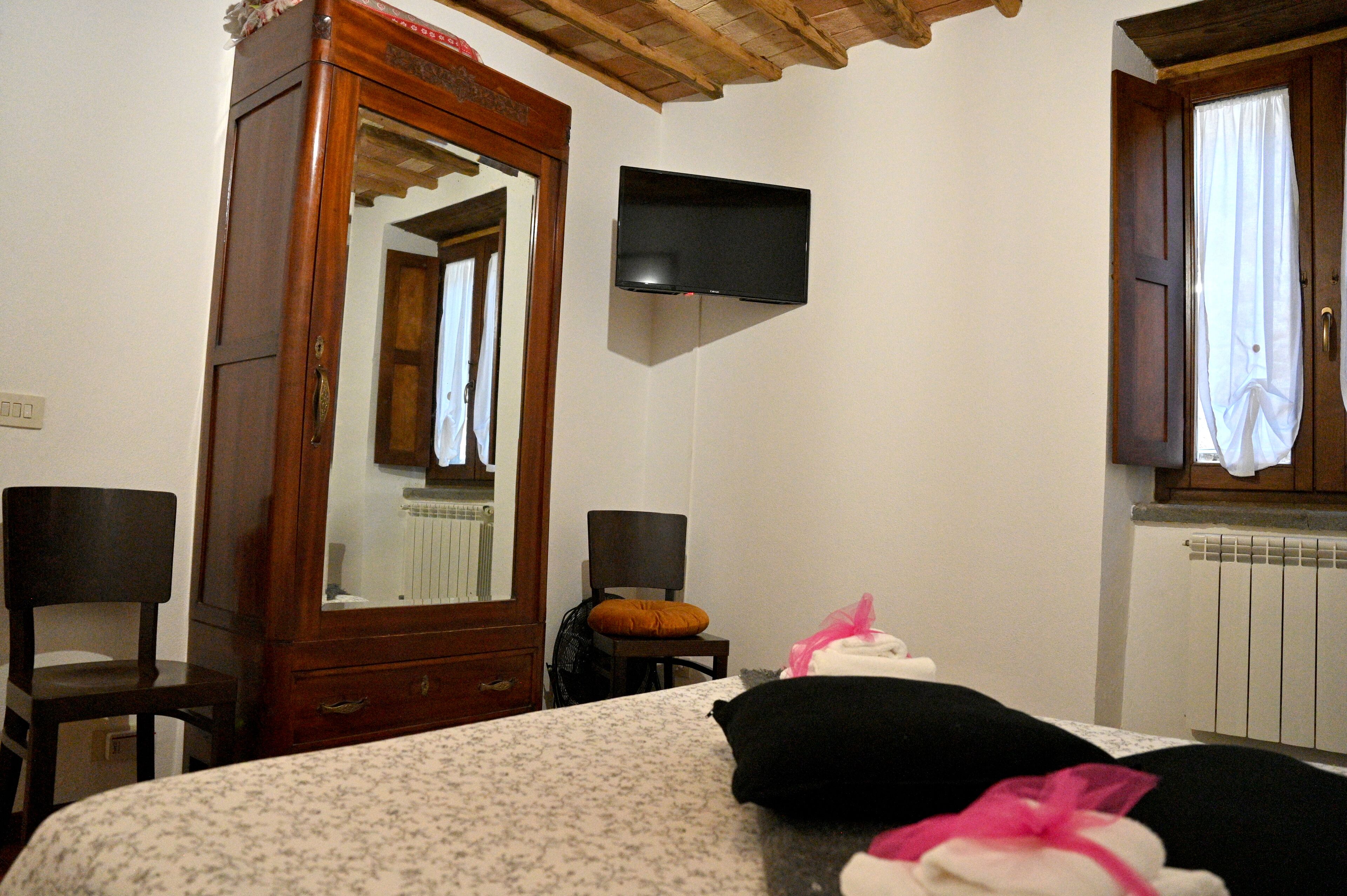 A bedroom with a wooden wardrobe, a bed with a floral bedspread, a black pillow, a white pillow, and a pink bow.
