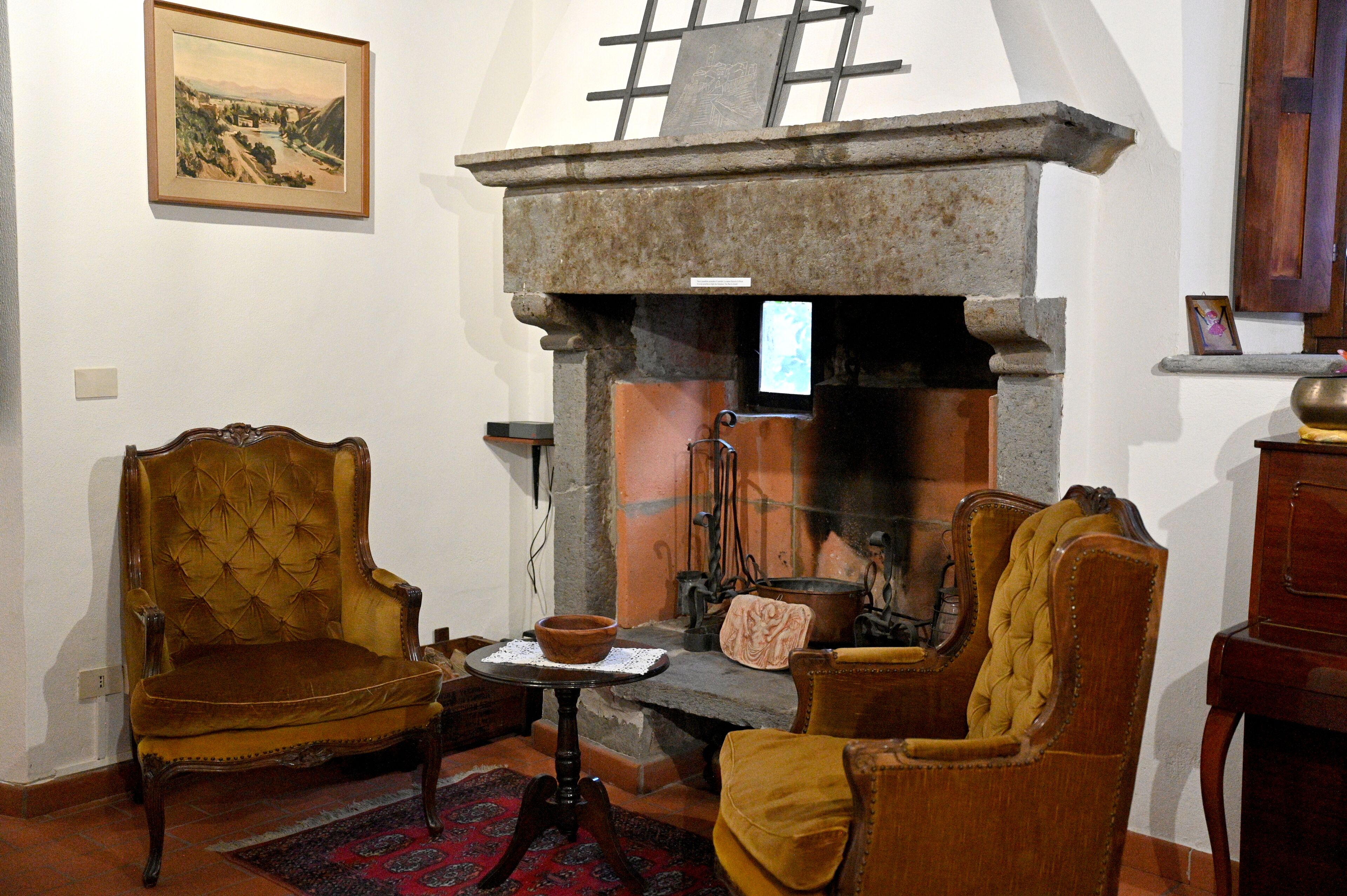 A traditional room with a stone fireplace, two upholstered chairs, a small table with a bowl, and a framed picture on the wall.