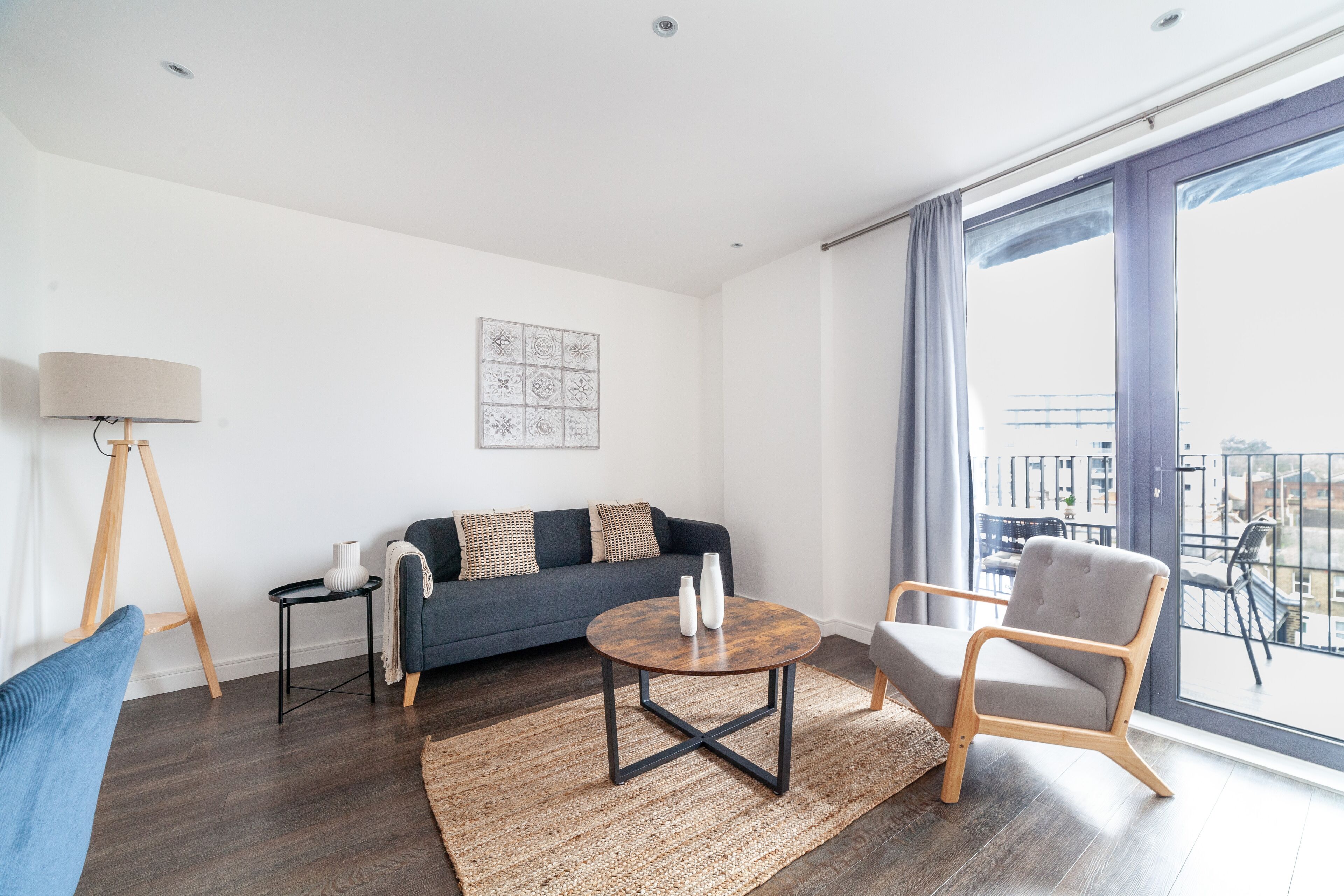 Un salon moderne avec un canapé gris foncé, une table basse ronde, un fauteuil en bois et une grande fenêtre donnant sur la ville.