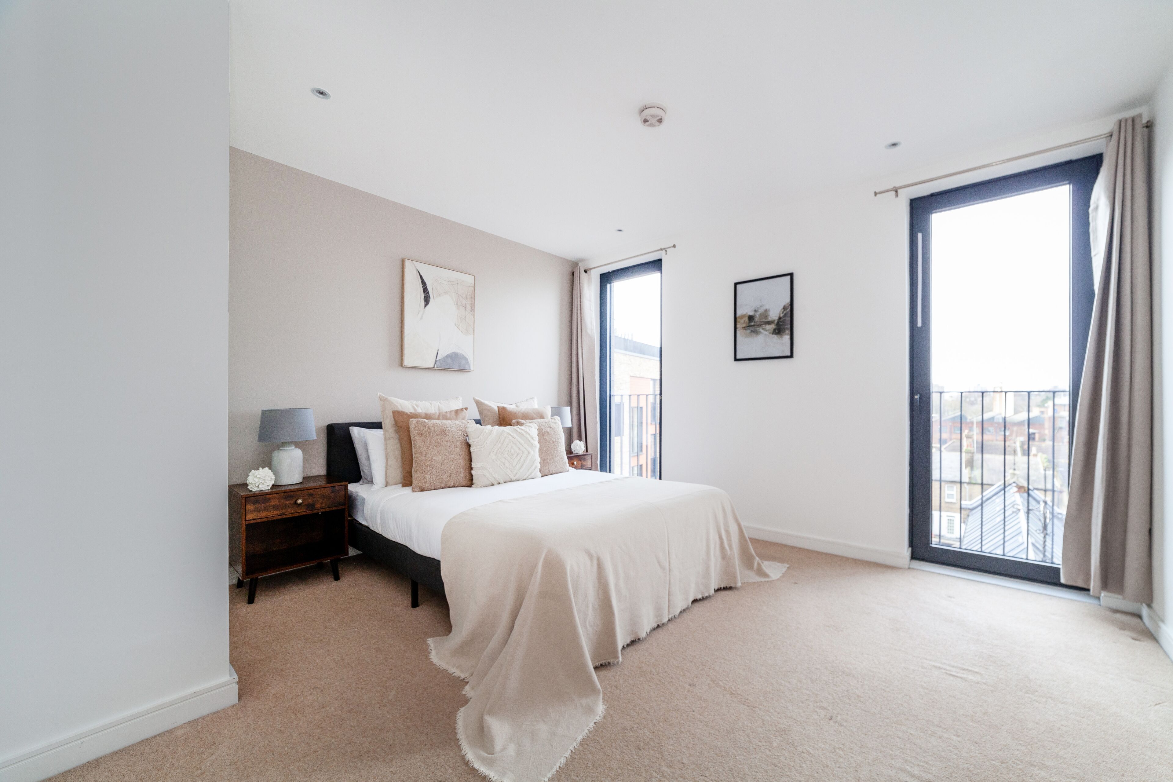 A bedroom with a large bed, a nightstand, a lamp, and a window with curtains.