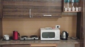 Ett litet kök med mikrovågsugn, vattenkokare och en gasspis. Det finns koppar och en termos på bänkskivan.