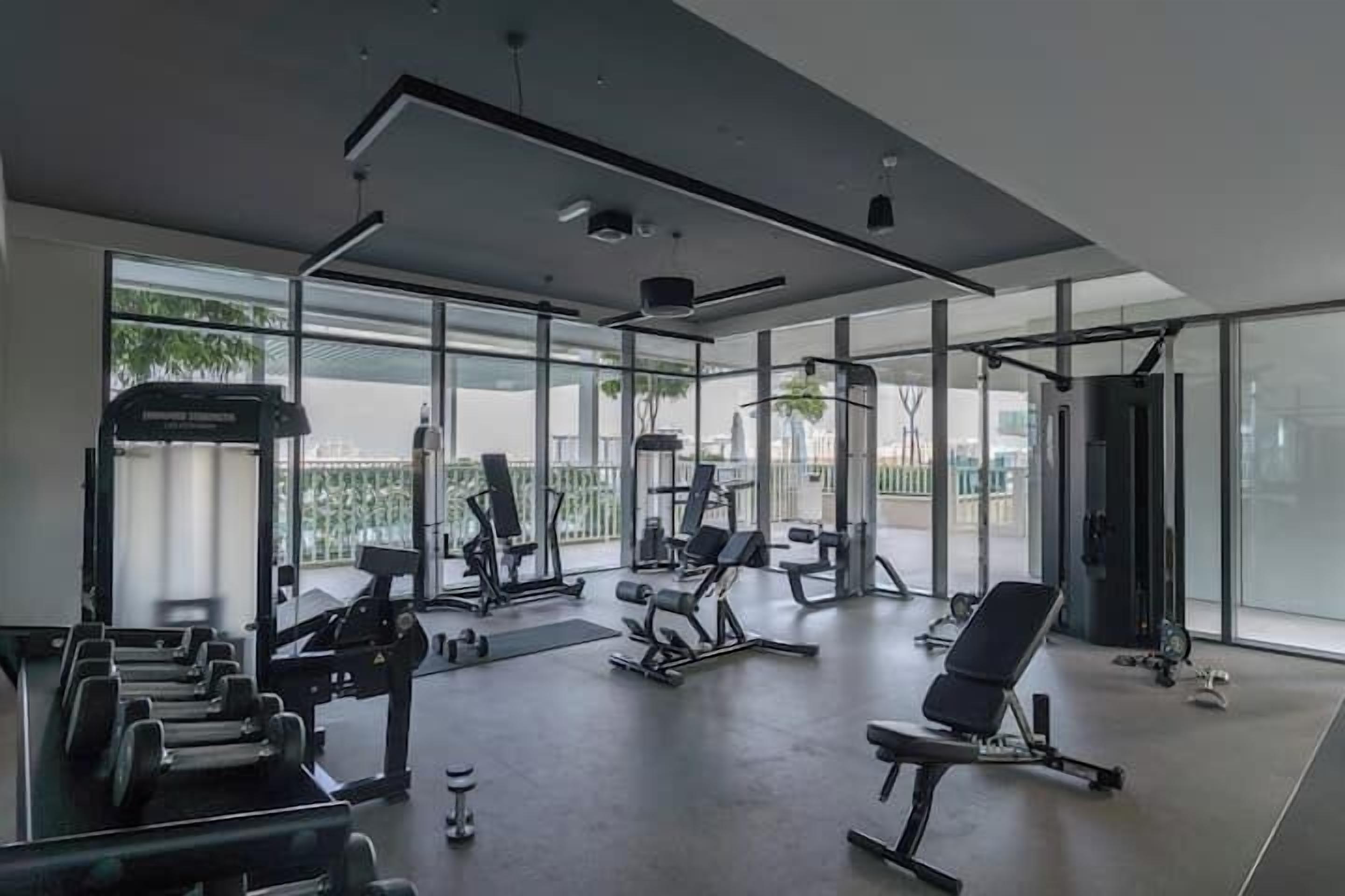 A modern gym with various exercise equipment, large windows, and a view of the city.