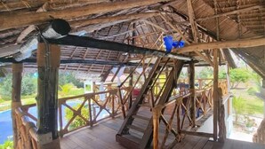 A wooden deck with a thatched roof, overlooking a pool and lush greenery.