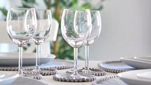 A dining table with four clear wine glasses and matching coasters, set against a backdrop of a green plant and a framed picture on the wall. - Immaculate 2-bed Apartment in London (London)