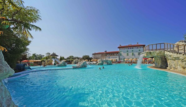 A large outdoor swimming pool with clear blue water, surrounded by rock formations and a building with a red roof.