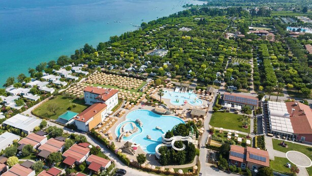 Vista aerea di un resort costiero con una grande piscina, diverse ville e vegetazione rigogliosa.