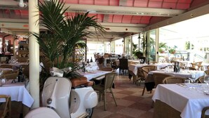 Un ristorante con posti a sedere all'aperto, tavoli con tovaglie bianche, sedie in vimini e un vecchio scooter.