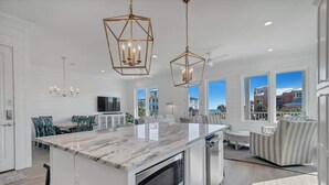 Une cuisine moderne dotée d’un grand îlot central, de luminaires suspendus et offrant une vue sur l’extérieur.