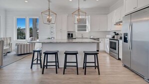 Une cuisine moderne avec des meubles blancs, un grand îlot central doté de tabourets, des appareils en acier inoxydable et un éclairage suspendu.