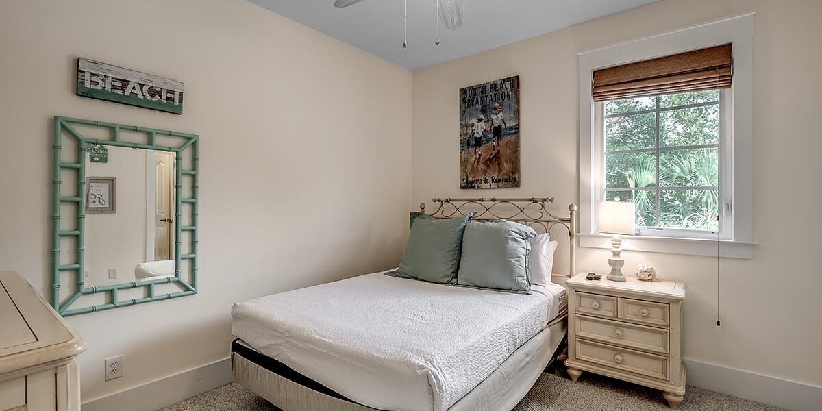 Une chambre avec un lit, une commode, une table de chevet, une fenêtre donnant sur un paysage verdoyant et une affiche accrochée au mur.