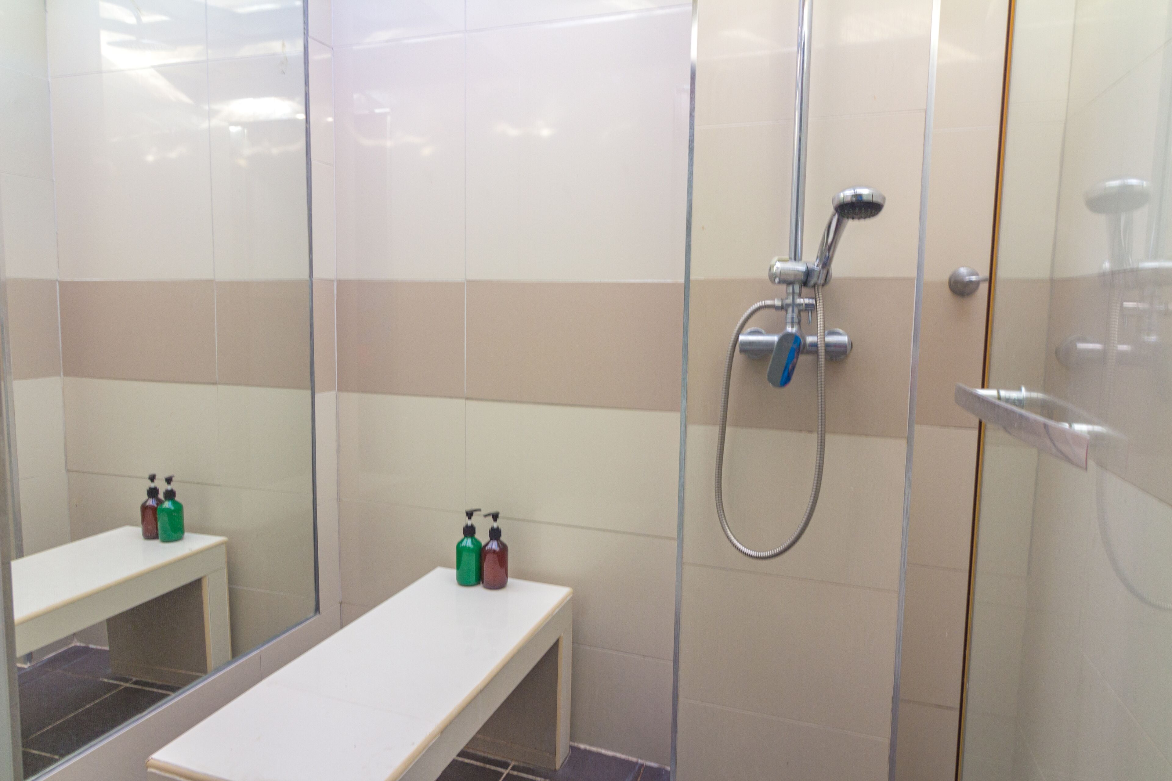 A bathroom with a glass shower enclosure, a bench, and two bottles of soap on a shelf.