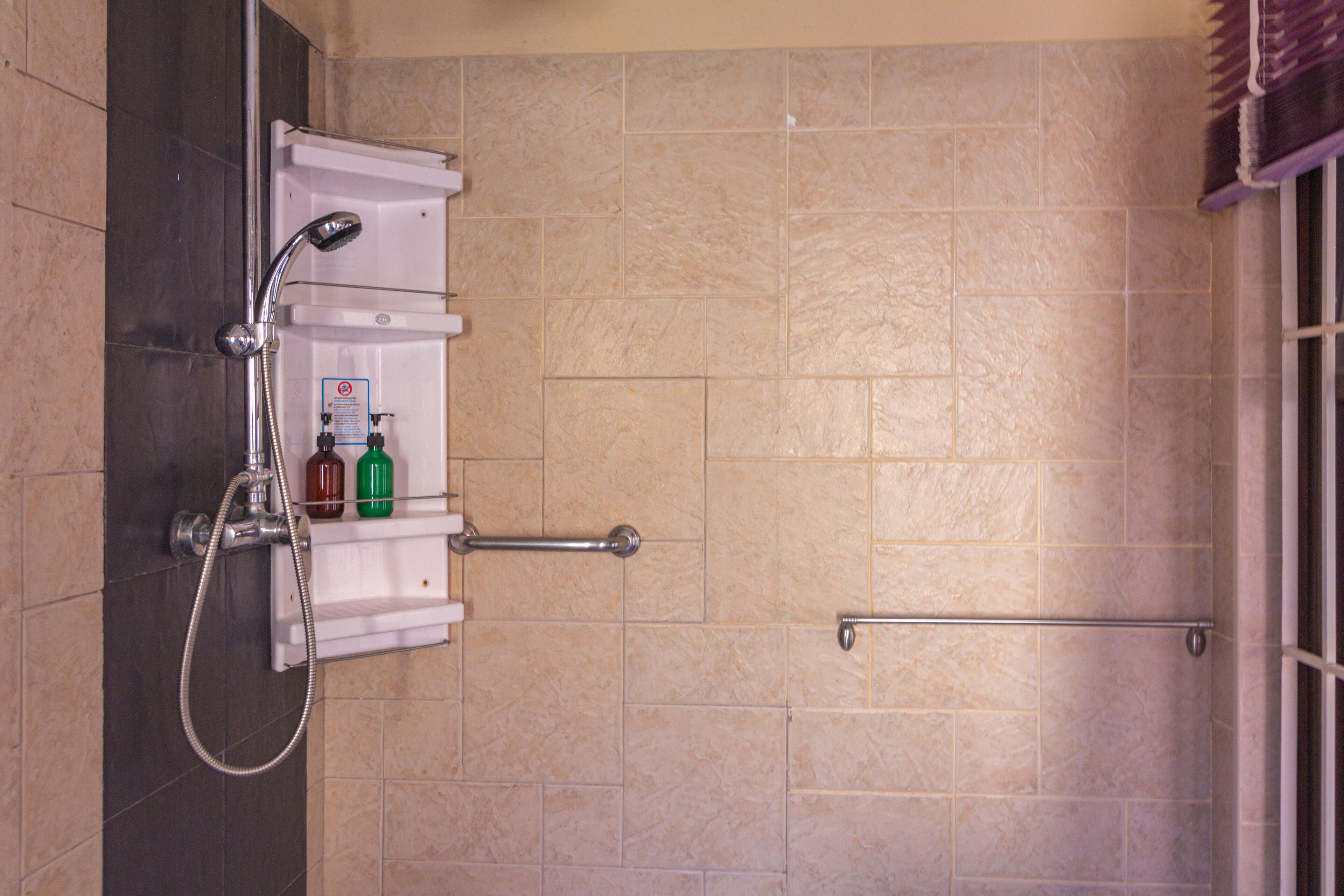 A shower area with a handheld showerhead, a soap dispenser, and a towel rack.