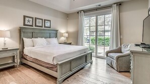 Ein Schlafzimmer mit einem großen Bett, zwei Nachttischen inklusive Lampen, einem Sessel und Blick ins Grüne durch ein großes Fenster.