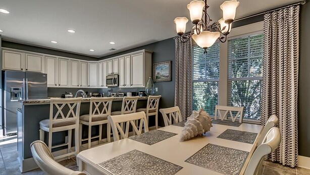 A modern kitchen with white cabinets, a stainless steel refrigerator, and a dining area with a white table and chairs.