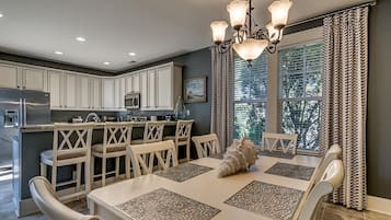 Een moderne keuken met witte kastjes, een roestvrijstalen koelkast, en een eethoek met een witte tafel en stoelen.