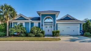 A two-story house with a garage, a central entrance with a glass door, and a small front yard with palm trees and shrubs.