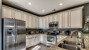 A modern kitchen with white cabinetry, stainless steel appliances, granite countertops, and a double sink.