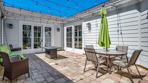 En overdækket terrasse med bord og stole, en skraldespand og en grøn parasol.