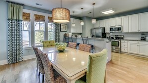 A modern kitchen with white cabinets, stainless steel appliances, and a dining area with a glass table and wicker chairs.
