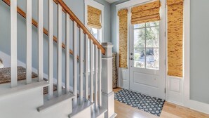 A staircase with white railings and wooden accents, a white door with a window, and a patterned doormat.