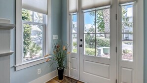 Un couloir avec deux portes blanches, une plante en pot et une fenêtre donnant sur un quartier résidentiel.