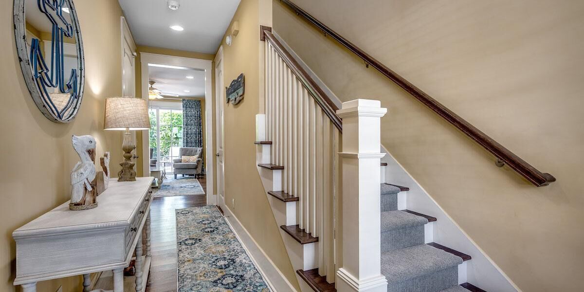 Un couloir avec un escalier, une console blanche ornée d’objets décoratifs et un tapis à motifs.