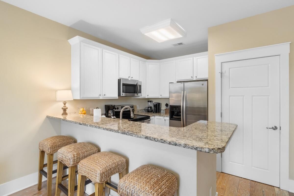 A kitchen with white cabinets, stainless steel appliances, a granite countertop, and three woven stools.