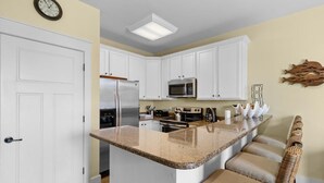 A kitchen with white cabinets, a stainless steel refrigerator, a microwave, and a granite countertop island with seating. - 1 Bedroom Carriage Home with Comfort and Style (North Myrtle Beach)