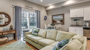 A cozy living room with a sofa, a dining table, and a kitchen area with cabinets and a window.