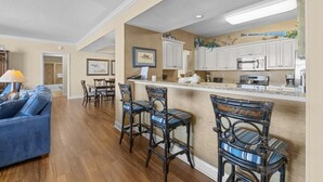 A kitchen with white cabinets, a microwave, and a bar area with chairs. - A Luxurious 5-Bedroom, 4.5-Bathroom Retreat for 14 (North Myrtle Beach)