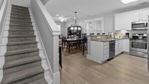 A modern kitchen with white cabinets, a stainless steel oven, and a dining area with a chandelier.