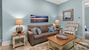 A living room with a brown sofa, two side tables with lamps, a coffee table, a patterned rug, a framed picture on the wall, and a chair with a cushion. - Elegant 1 Bdrm Flat: Your Ultimate Retreat for 4 (North Myrtle Beach)