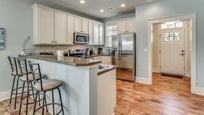 Una cocina con armarios blancos, un refrigerador de acero inoxidable y una barra con taburetes.