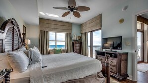 A spacious bedroom with a large bed, a ceiling fan, a television, and a view of the ocean. - Luxury Oceanfront 4 Bedroom Condo: Sleeps 12 (North Myrtle Beach)
