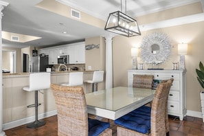 A modern kitchen with white cabinets, a stainless steel refrigerator, and a dining area with a glass table and wicker chairs.