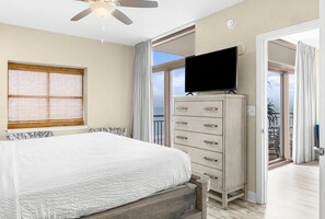 Ein Schlafzimmer mit Bett, Fernseher auf einer Kommode, Deckenventilator und Blick ins Freie.