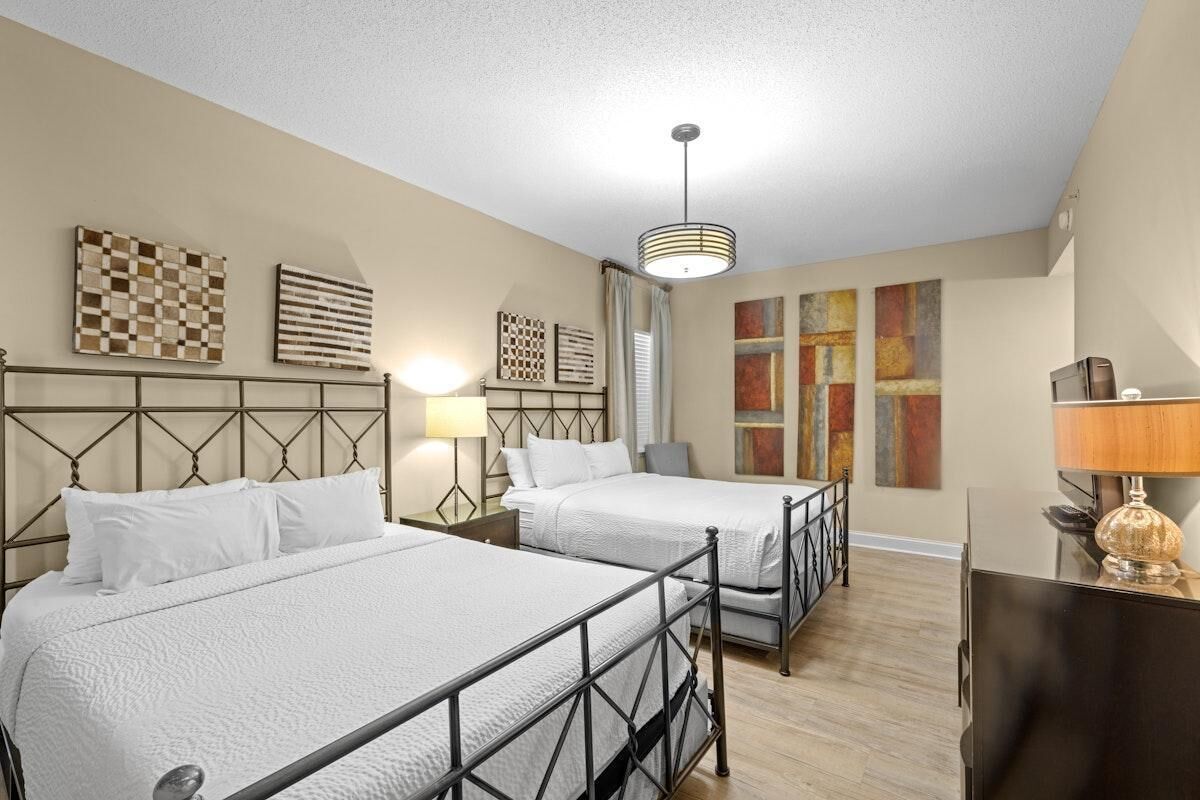 Habitación de hotel con dos camas, televisión y obras de arte en las paredes.
