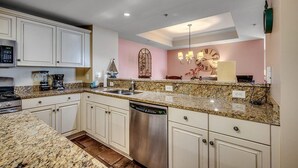 A kitchen with white cabinets, granite countertops, a dishwasher, and a coffee maker. - Unparalleled Luxury in Our Exquisite 4 Bdrm Condo (North Myrtle Beach)