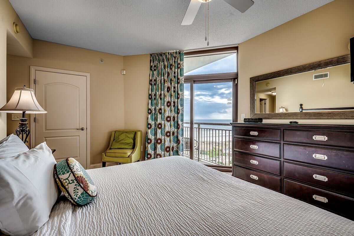 Une chambre avec un lit, une commode, une chaise et un balcon offrant une vue.