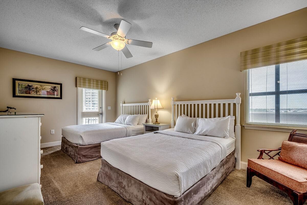 Une chambre d’hôtel avec deux lits, un ventilateur de plafond, une fenêtre avec des stores, une chaise et un bureau avec une lampe.