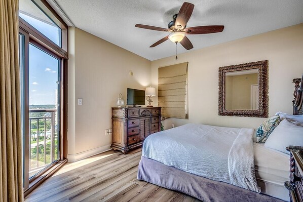 A bedroom with a large bed, a ceiling fan, a dresser, a mirror, and a window with a view. - Unwind in Luxury : Oceanfront 4 Bedroom Condo (North Myrtle Beach)