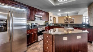 A modern kitchen with stainless steel appliances, dark wood cabinets, a central island, and a chandelier. - Unwind in Luxury : Oceanfront 4 Bedroom Condo (North Myrtle Beach)