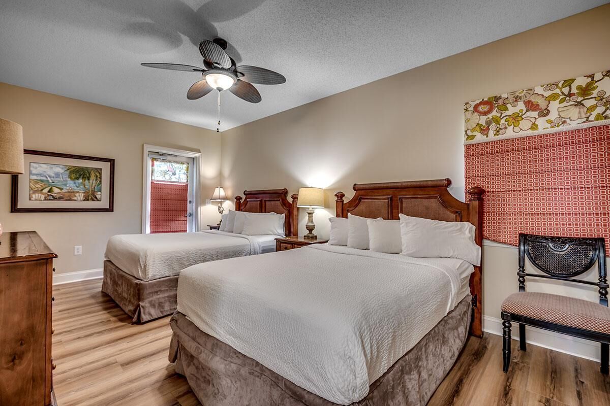 A hotel room with two beds, a ceiling fan, a wooden headboard, a chair, and a wall with a floral pattern.