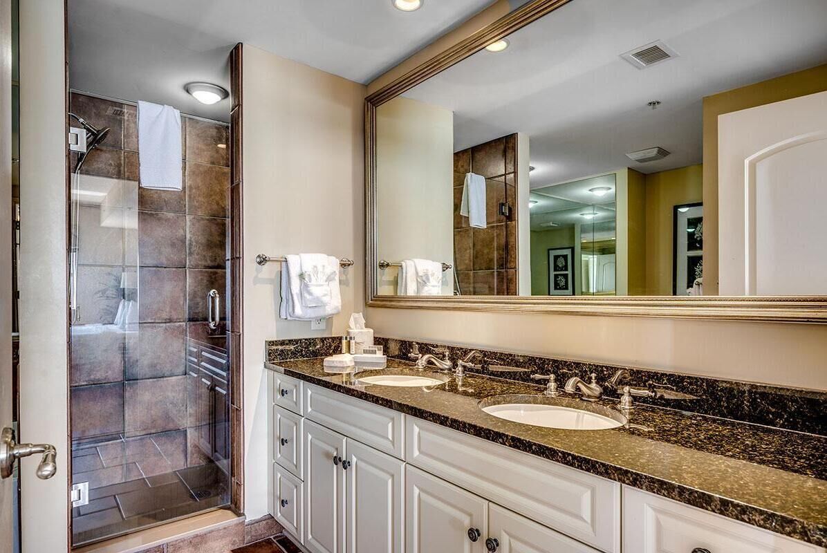 Un baño moderno con dos lavamanos, un espejo grande y una ducha con cerramiento de vidrio.