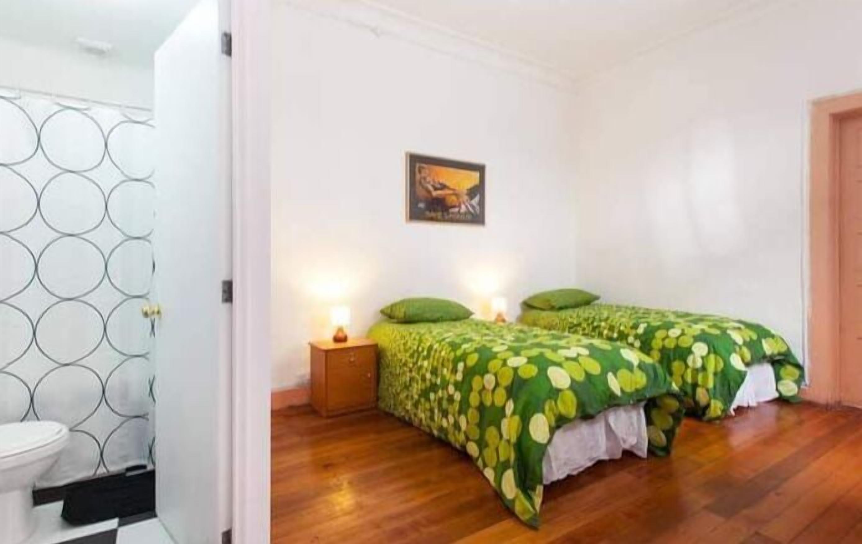 A bedroom with two beds, a nightstand, a wall-mounted picture, and a wooden floor.