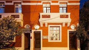Un edificio con fachada tradicional, un cartel anunciador y un pequeño jardín con una banca.