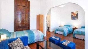 Una habitación con dos camas, un sofá, un armario de madera y una mesa de vidrio.