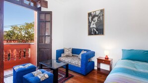 Una habitación con un sofá azul, una cama, una mesita y un cuadro colgado en la pared.