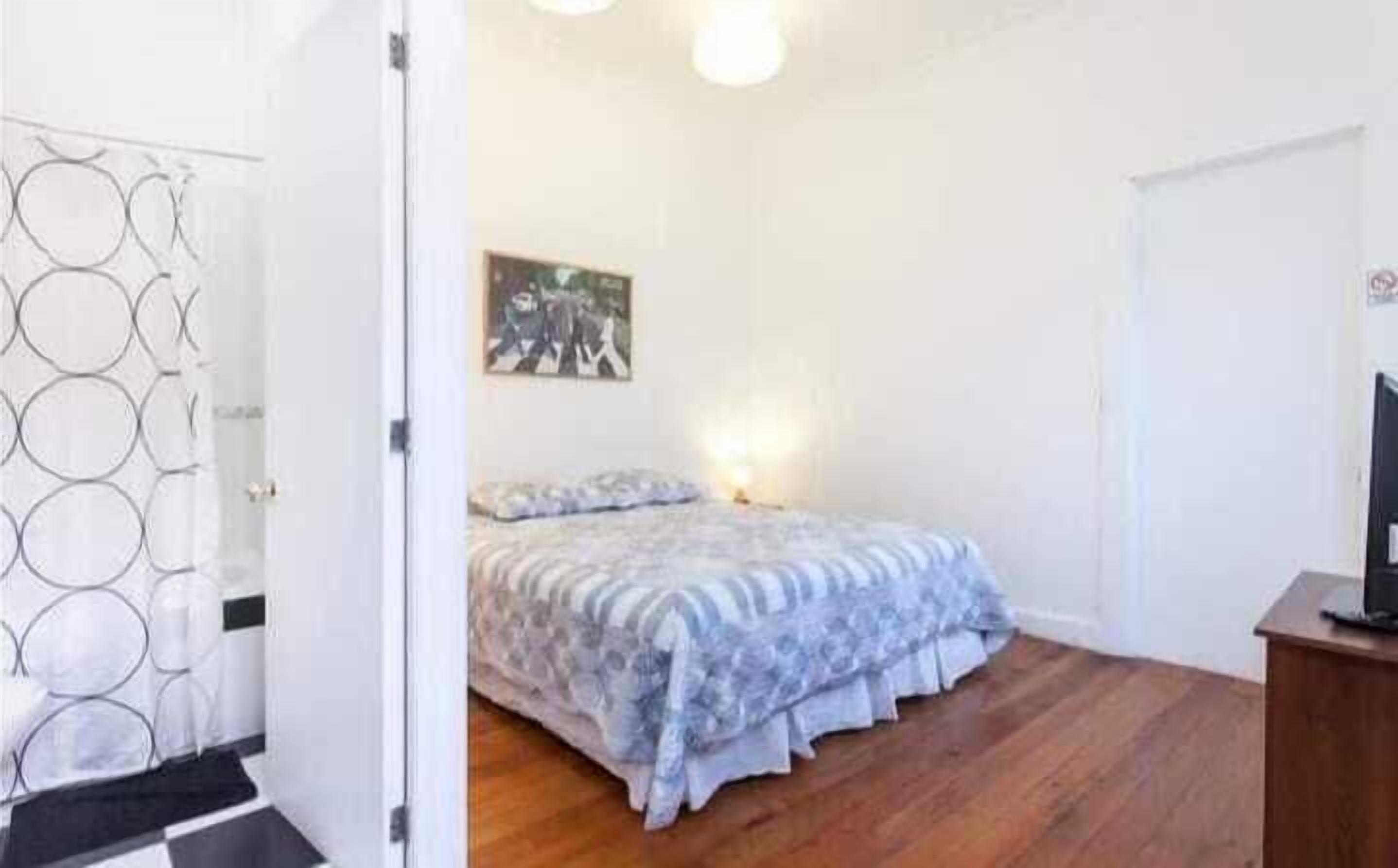 A bedroom with a bed, a painting on the wall, and a wooden floor.
