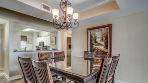 A dining area with a glass-top table, wooden chairs, and a chandelier. - Seaside Splendor: Oceanfront Four Bedroom Gem (North Myrtle Beach)